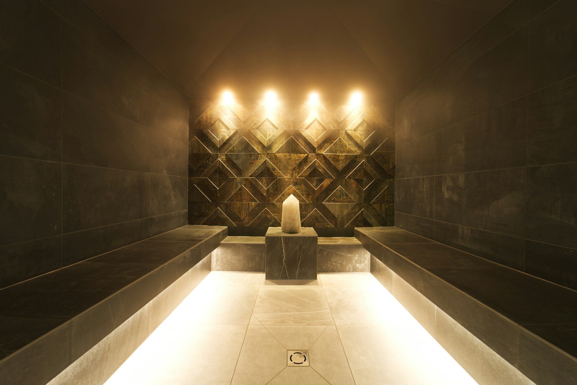 A softly lit stone steam room with warm ambient lighting for herbal steam therapy.