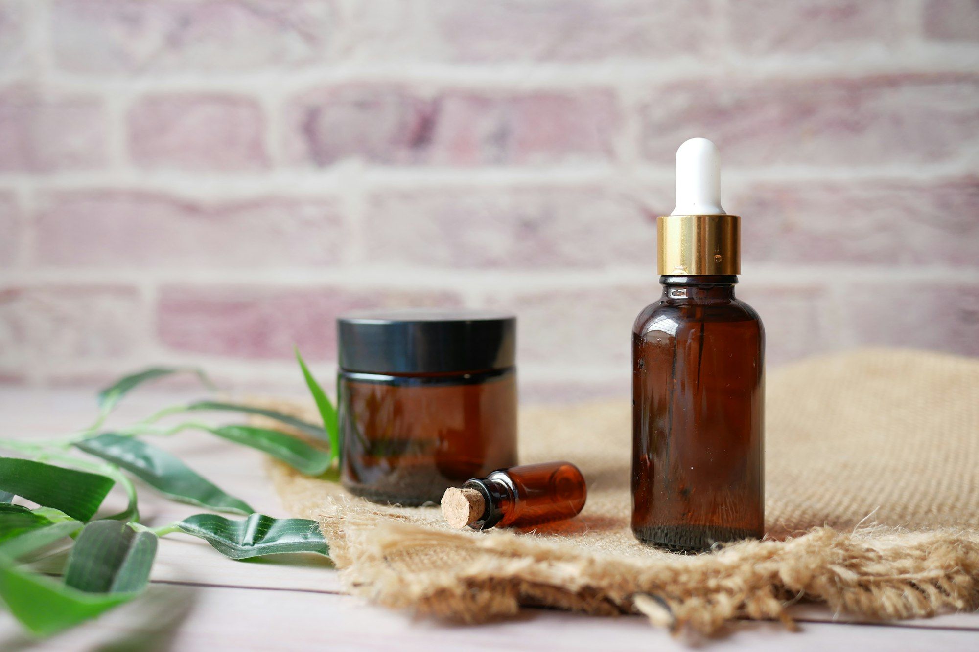 Amber glass bottles of medicated oil with green leaves on a natural jute cloth.