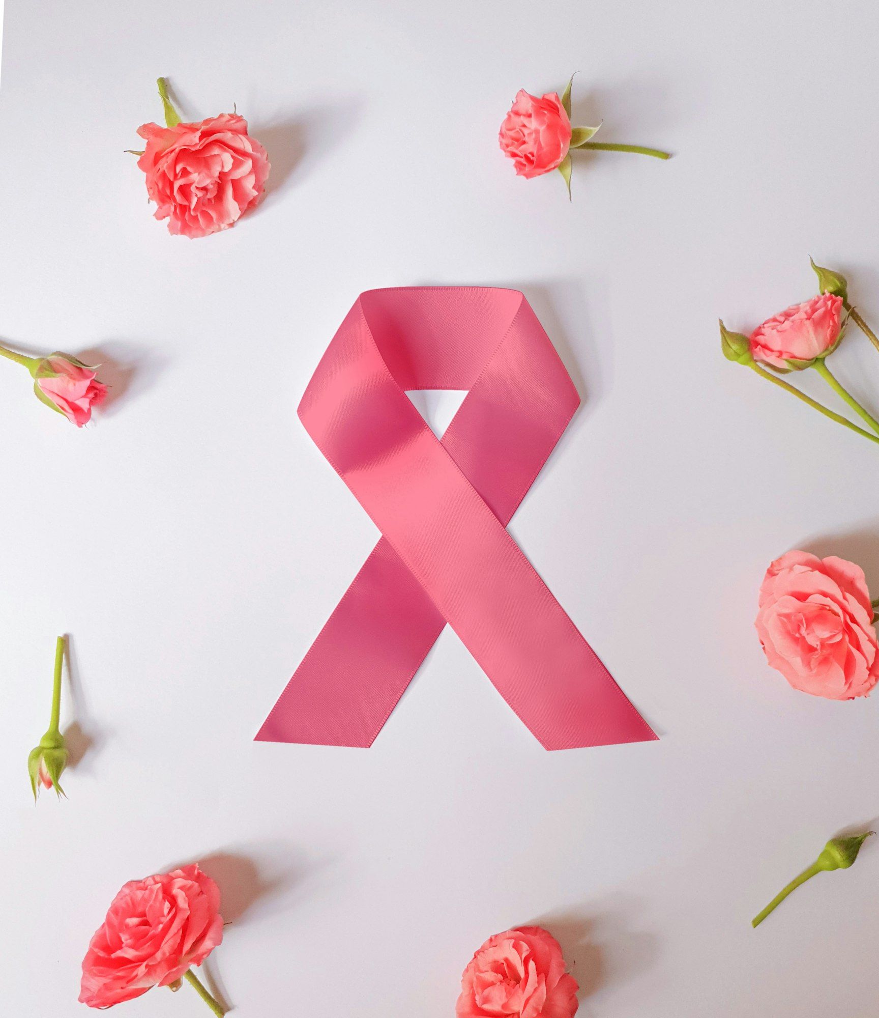 A pink awareness ribbon surrounded by small pink roses on a white background.