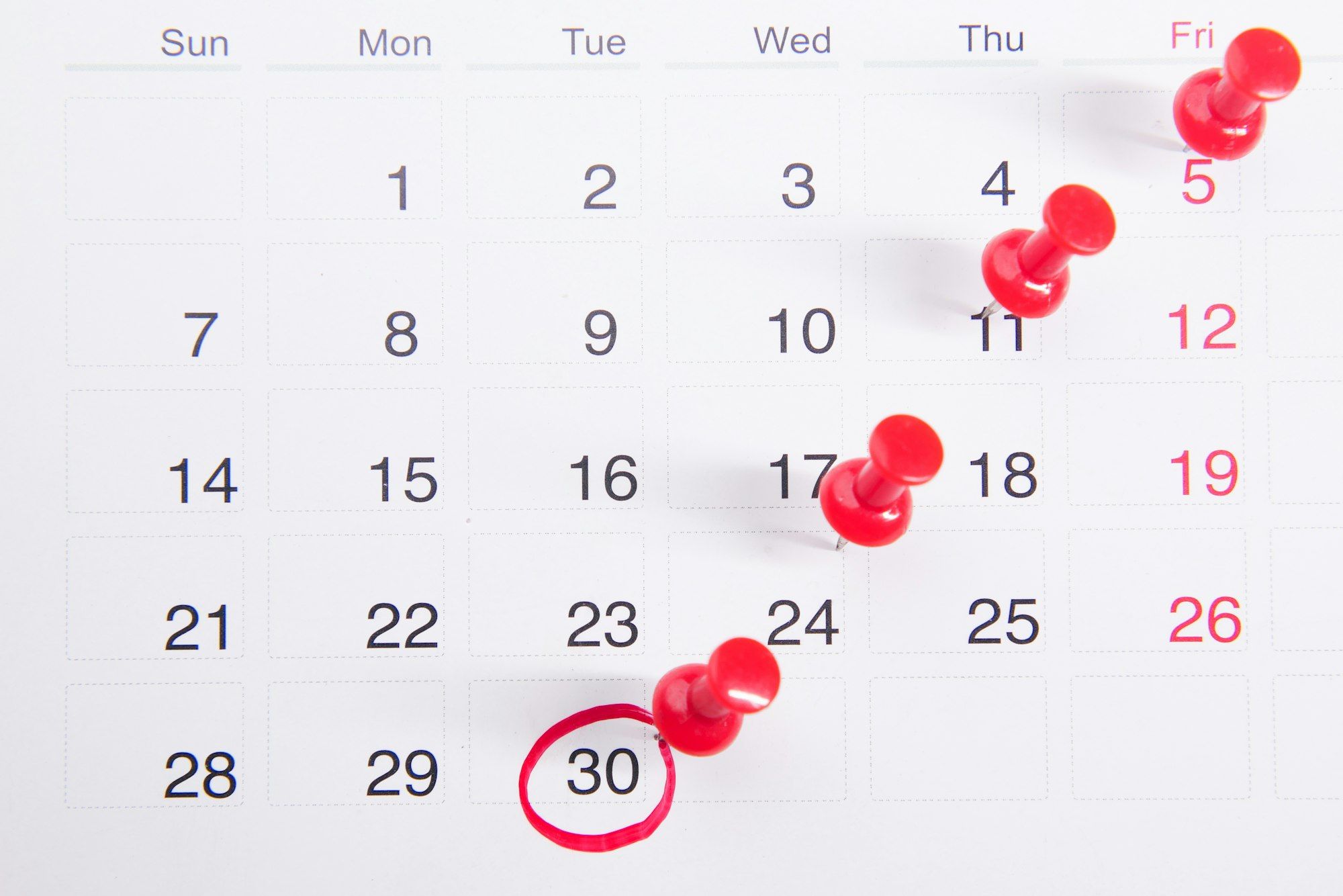 A monthly calendar with red push pins marking dates and one date circled in red.