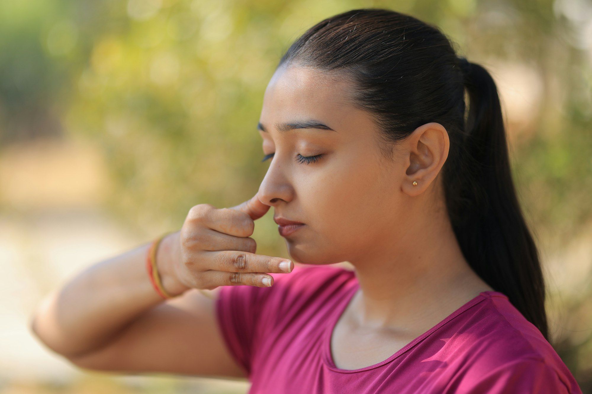 A young Indian woman with eyes closed gently closes one nostril during a calming breathing practice.