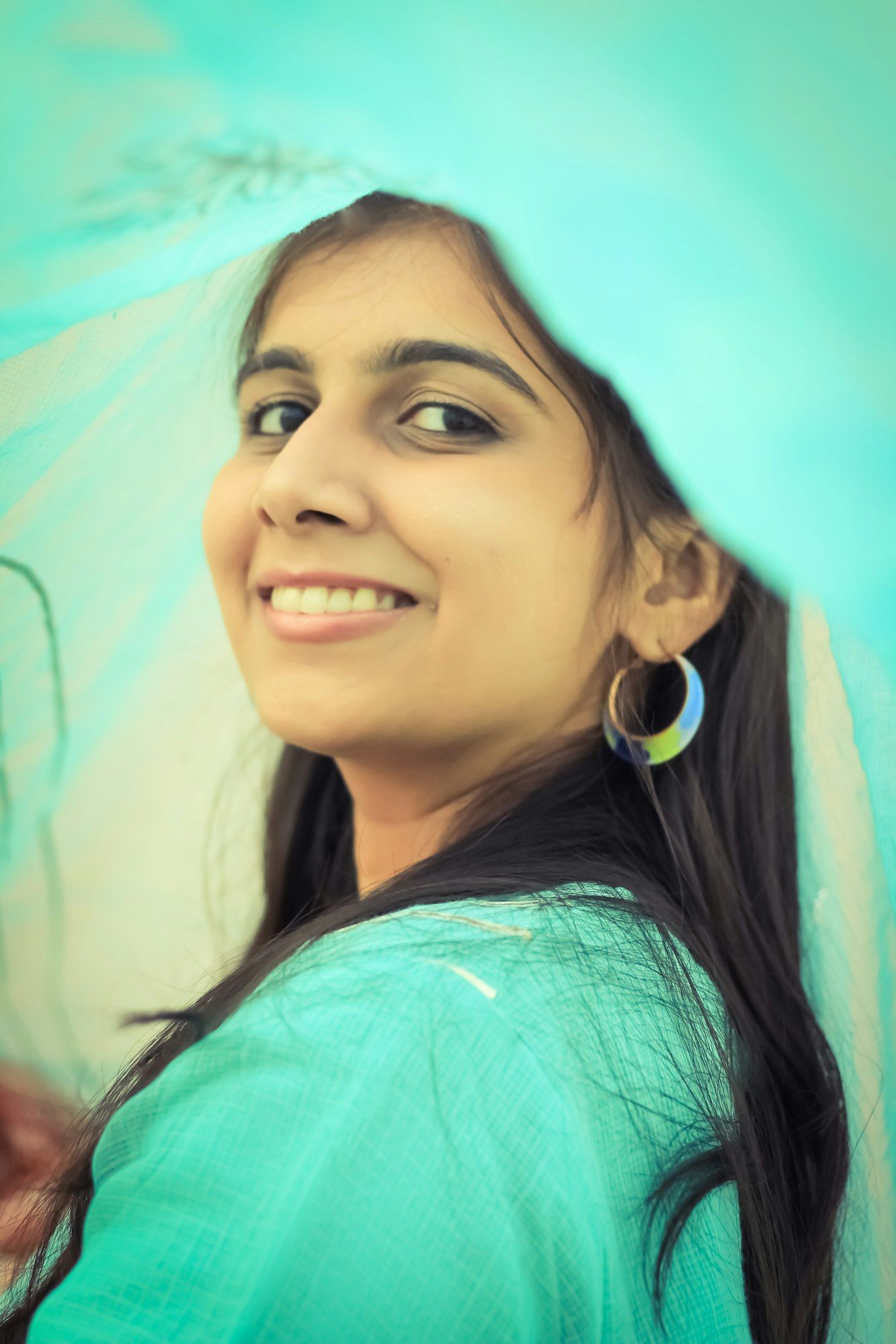 A smiling young Indian woman in a teal kurta and dupatta glancing back over her shoulder.