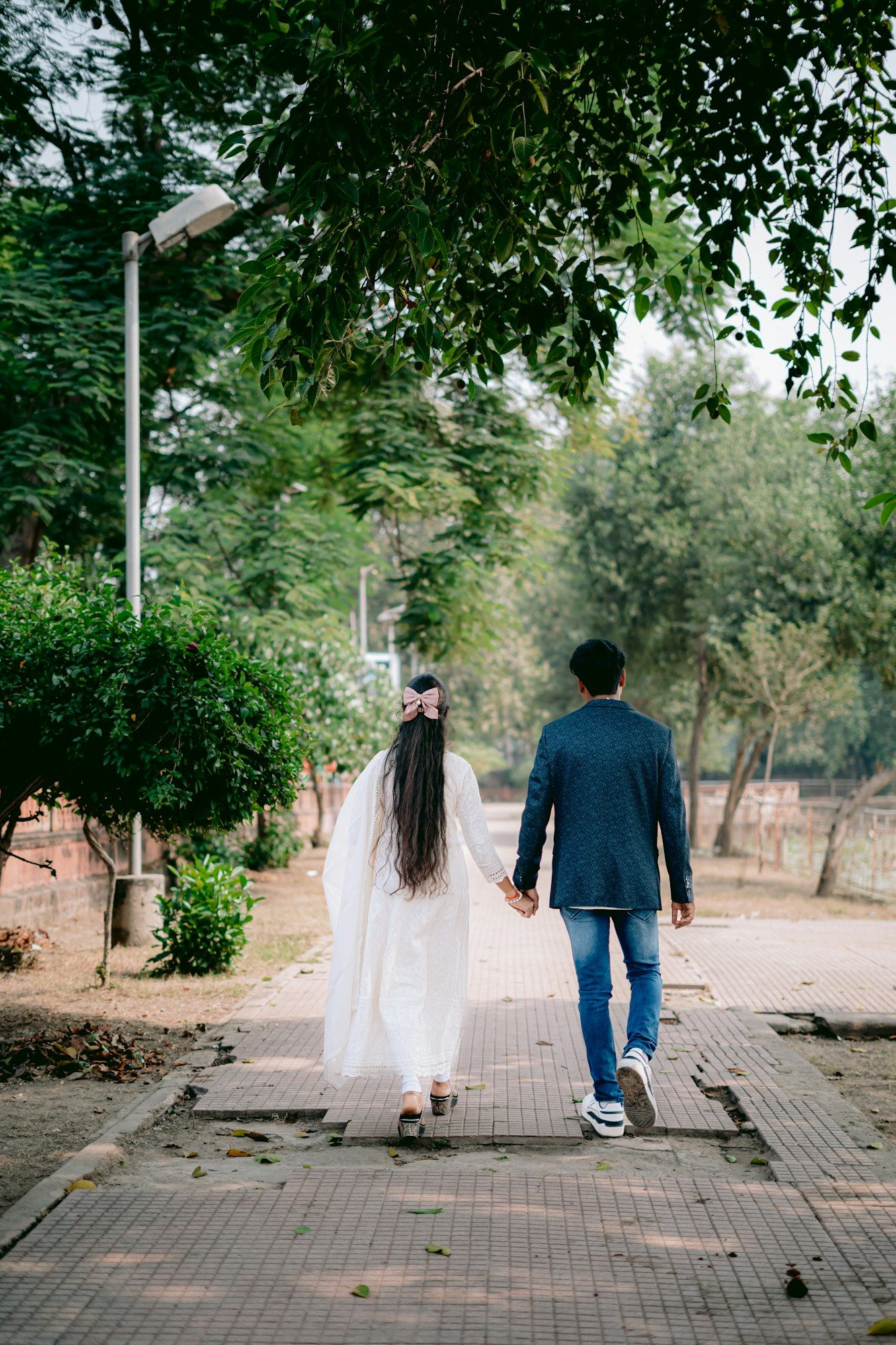 An Indian couple walking hand in hand along a tree-lined park path.