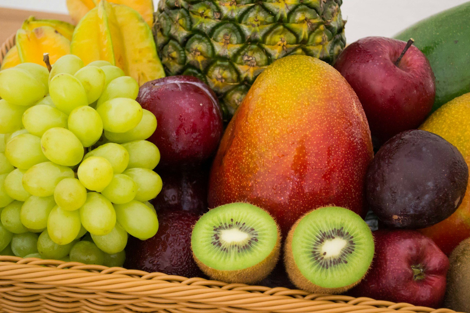 A basket of fresh fruit including grapes, mango, pineapple, kiwi and plums.