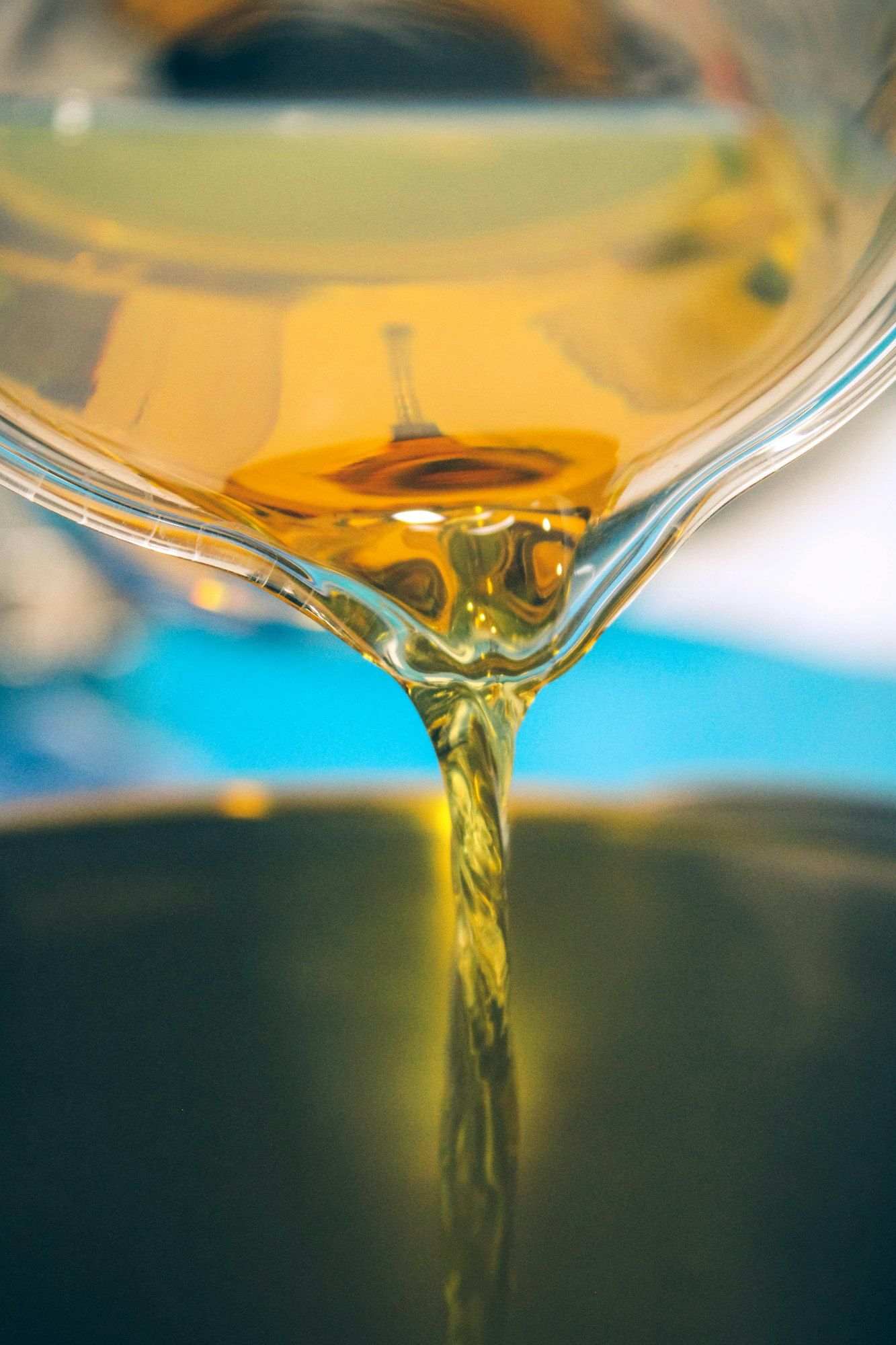 A slow, steady stream of golden oil pours from a glass vessel.