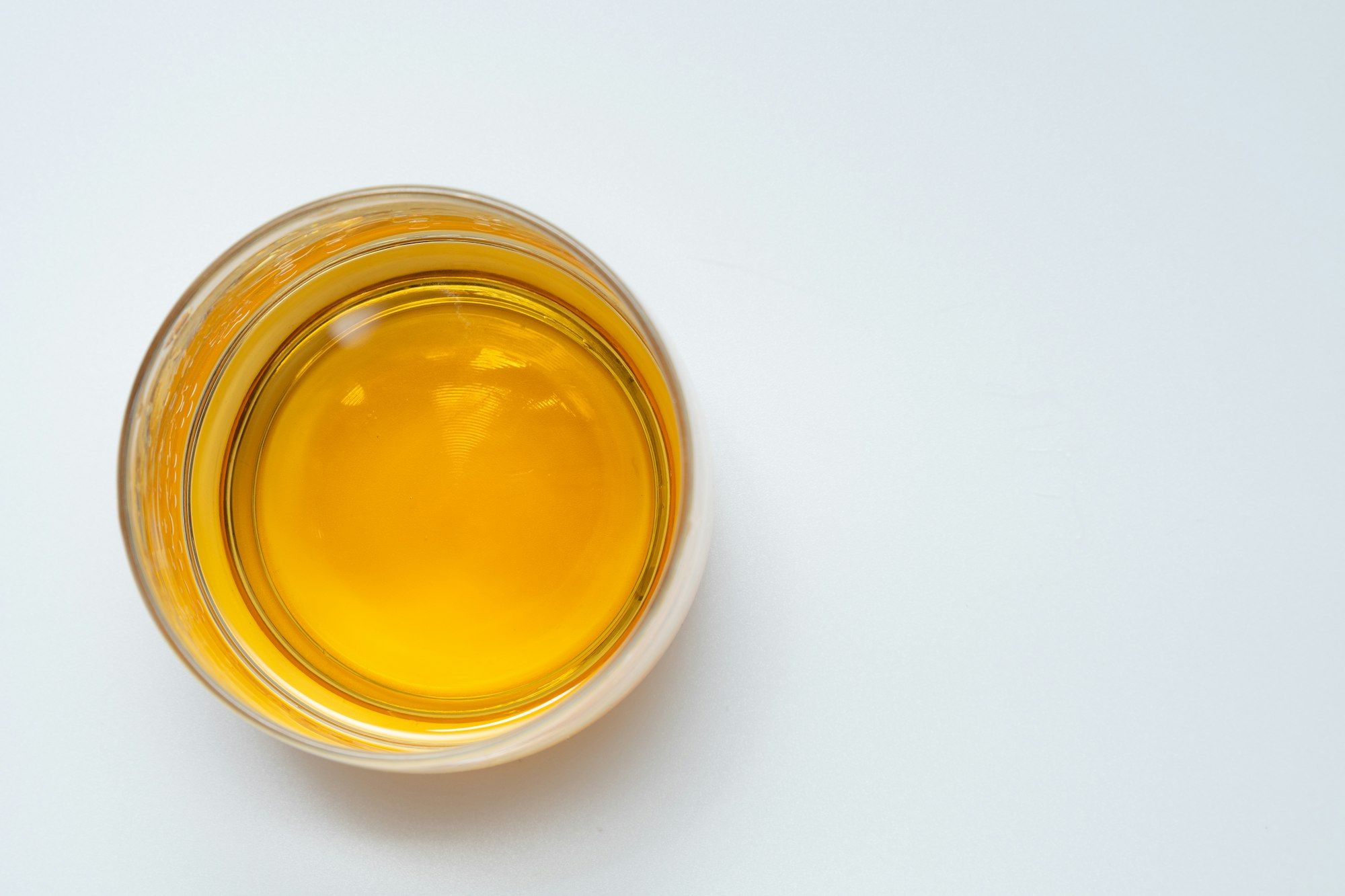 A small glass bowl of golden herbal oil on a clean pale surface.