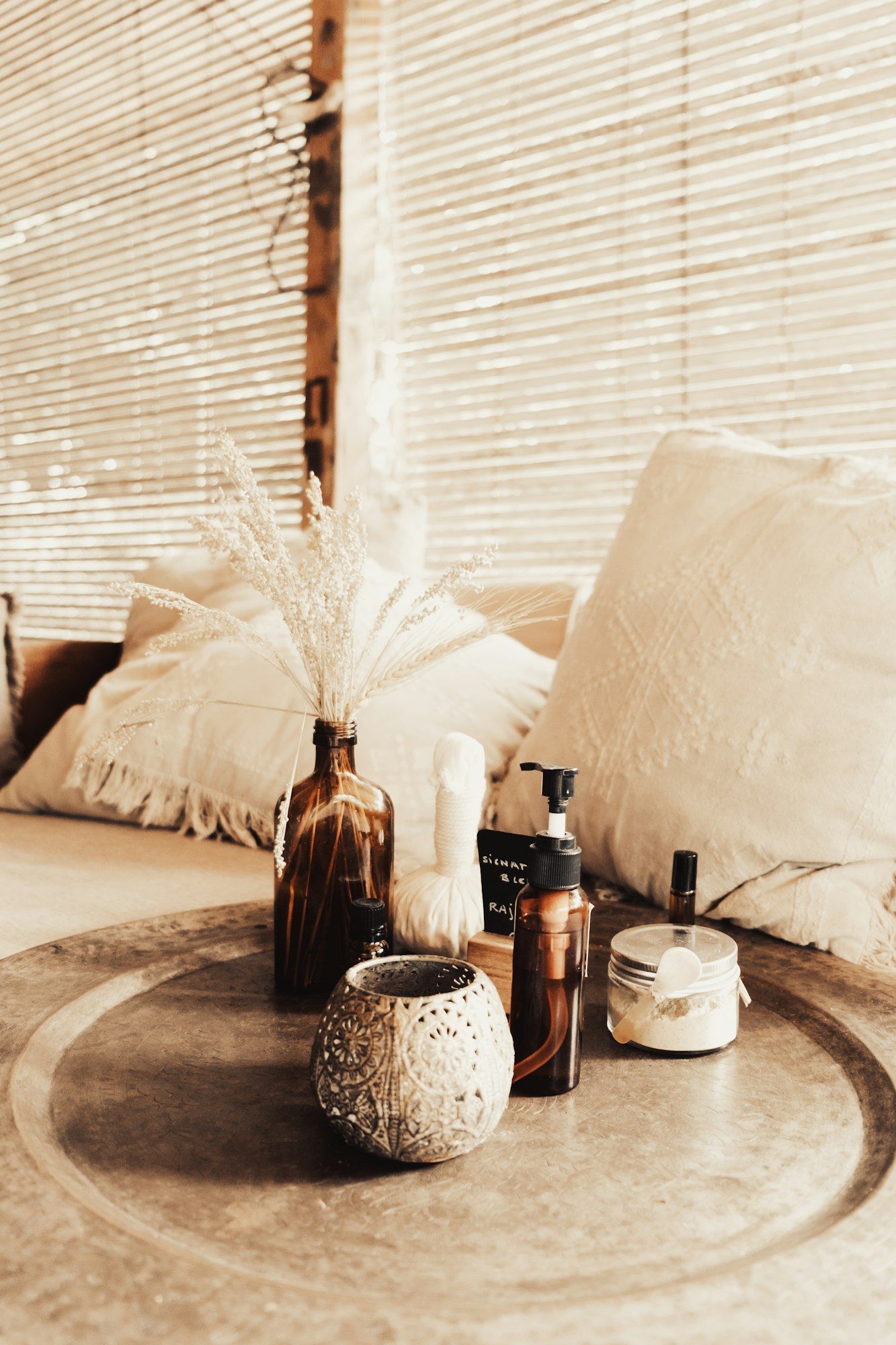 A calm treatment-room still life of amber oil bottles, a herbal compress and dried grasses on a brass tray.