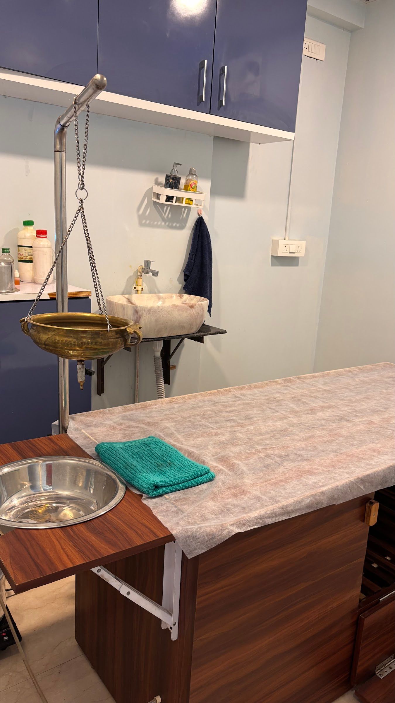 The Panchakarma room with a brass Shirodhara vessel above a wooden therapy table
